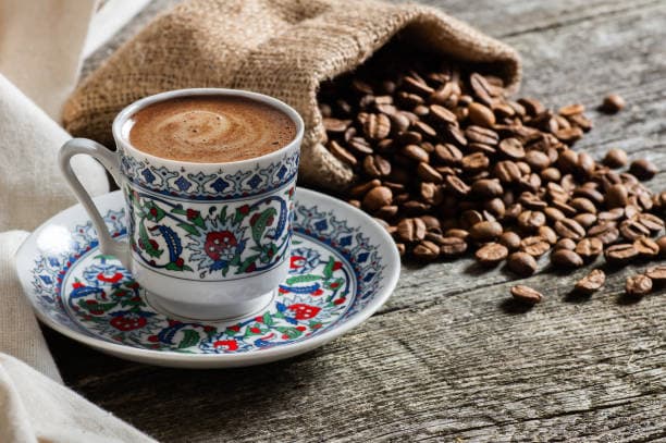 فنجان قهوة تركية مزخرف بجانب كيس من حبوب القهوة